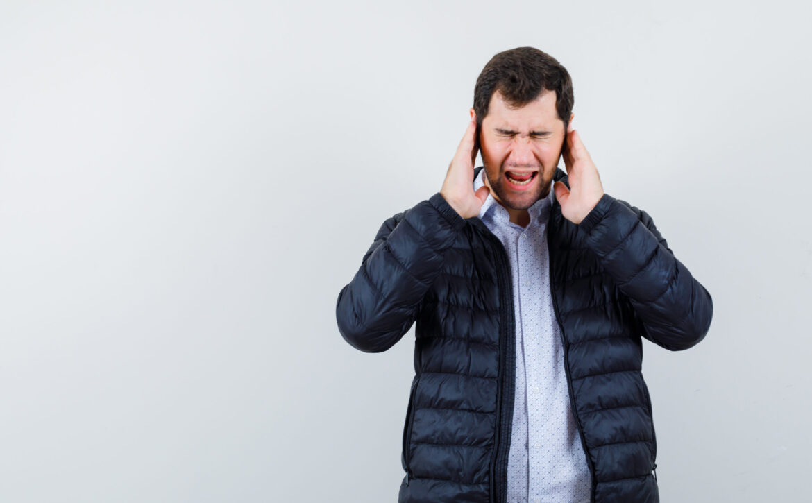 The young man is closing his ears with hands on white background